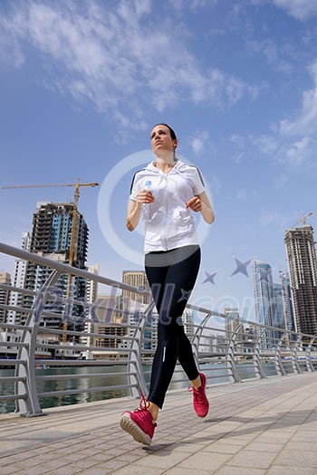 Running in city park. Woman runner outside jogging at morning with Dubai urban scene in background Running in city park. Woman runner outside jogging at morning with Dubai urban scene in background
