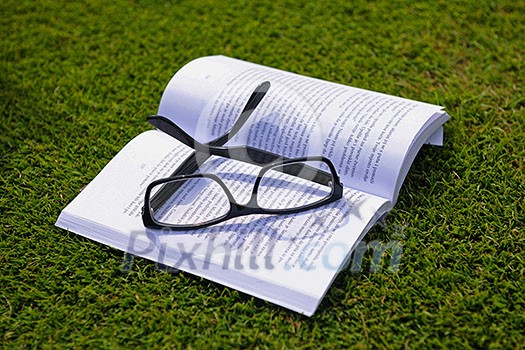 Glasses on a book outside with grass inbbacground, education relax and study concept Glasses on a book outside with grass inbbacground, education relax and study concept