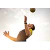 Young, male man playing soccer (lit by warm evening sunlight) heading the ball in the air