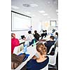 People listening to a presentation in a modern, bright meeting room (shallow DOF; color toned image)