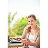 Portrait of a pretty young woman working on her computer on a terrace of her house - paying online with her credit card