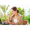 Portrait of a pretty young woman working on her computer on a terrace of her house - paying online with her credit card