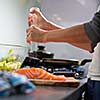 Young woman seasoning a salomn filet in her modern kitchen, preaparing a healthy food