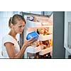 Is this still fine? Pretty, young woman in her kitchen by the fridge, looking at the expiry date of a product she took from her fridge -