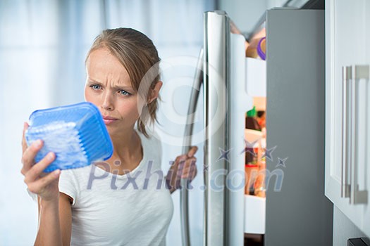 Is this still fine? Pretty, young woman in her kitchen by the fridge, looking at the expiry date of a product she took from her fridge -