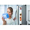 Is this still fine? Pretty, young woman in her kitchen by the fridge, looking at the expiry date of a product she took from her fridge -