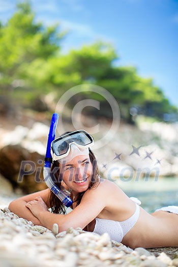 Pretty, young woman on a beach during her summer vacation with snorkel lying on beach with snorkeling mask and fins smiling happy enjoying the sun on a sunny summer day. Pretty, young woman on a beach during her summer vacation with snorkel lying on beach with snorkeling mask and fins smiling happy enjoying the sun on a sunny summer day.