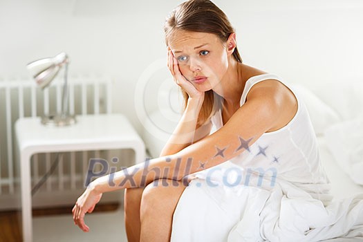 Pretty, young woman sitting on bed looking unhappy, depressed, feeling burnout, lacking motivation to get up and do what is expected from her Pretty, young woman sitting on bed looking unhappy, depressed, feeling burnout, lacking motivation to get up and do what is expected from her