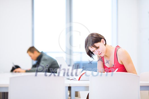 Pretty, young college student studying in the library/a study room at campus , using her modern laptop computer, writing notes, preparing for exams (shallow DOF) Pretty, young college student studying in the library/a study room at campus , using her modern laptop computer, writing notes, preparing for exams (shallow DOF)