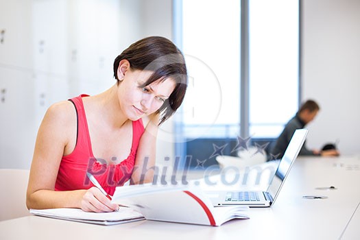 Pretty, young college student studying in the library/a study room at campus , using her modern laptop computer, writing notes, preparing for exams (shallow DOF) Pretty, young college student studying in the library/a study room at campus , using her modern laptop computer, writing notes, preparing for exams (shallow DOF)