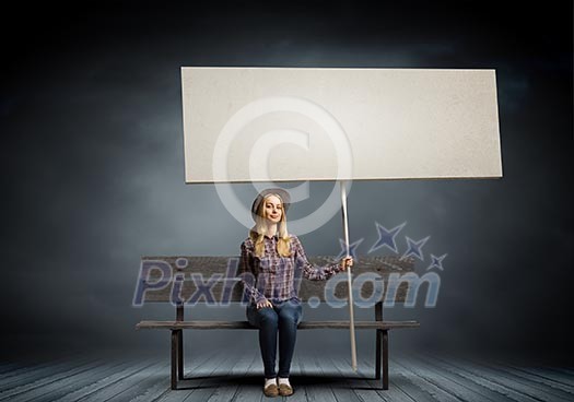 Young woman in casual sitting on bench and holding white blank banner Young woman in casual sitting on bench and holding white blank banner