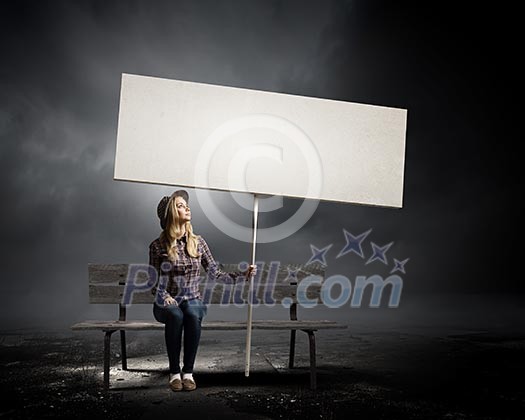 Young woman in casual sitting on bench and holding white blank banner Young woman in casual sitting on bench and holding white blank banner