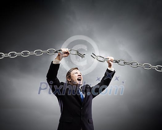 Young furious businessman breaking metal chain with hands Young furious businessman breaking metal chain with hands