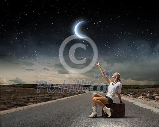 Young woman sitting on briefcase along roadside Young woman sitting on briefcase along roadside