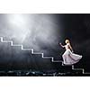 Young woman in white long dress walking up the staircase