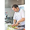 Handsome chef dressed in white uniform decorating pasta salad and seafood fish in modern kitchen