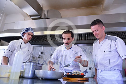 Handsome chef dressed in white uniform decorating pasta salad and seafood fish in modern kitchen Handsome chef dressed in white uniform decorating pasta salad and seafood fish in modern kitchen