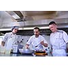 Handsome chef dressed in white uniform decorating pasta salad and seafood fish in modern kitchen