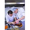 Handsome chef dressed in white uniform decorating pasta salad and seafood fish in modern kitchen