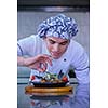 Handsome chef dressed in white uniform decorating pasta salad and seafood fish in modern kitchen