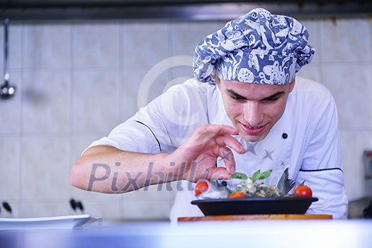 Handsome chef dressed in white uniform decorating pasta salad and seafood fish in modern kitchen Handsome chef dressed in white uniform decorating pasta salad and seafood fish in modern kitchen