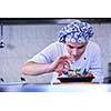 Handsome chef dressed in white uniform decorating pasta salad and seafood fish in modern kitchen