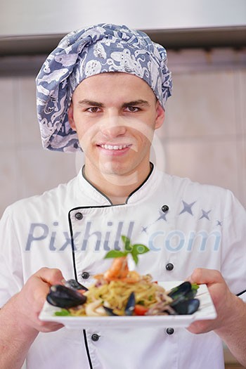 Handsome chef dressed in white uniform decorating pasta salad and seafood fish in modern kitchen Handsome chef dressed in white uniform decorating pasta salad and seafood fish in modern kitchen