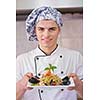 Handsome chef dressed in white uniform decorating pasta salad and seafood fish in modern kitchen