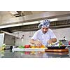 Handsome chef dressed in white uniform decorating pasta salad and seafood fish in modern kitchen