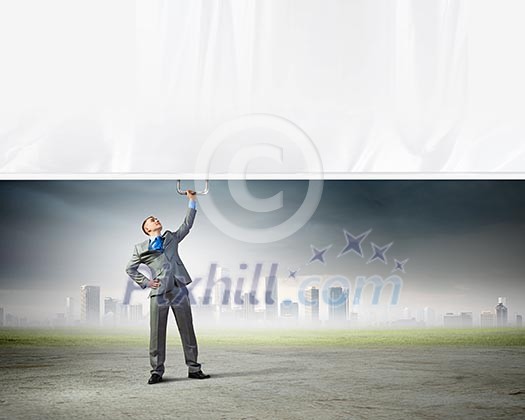 Image of young businessman pulling blank banner from above Image of young businessman pulling blank banner from above
