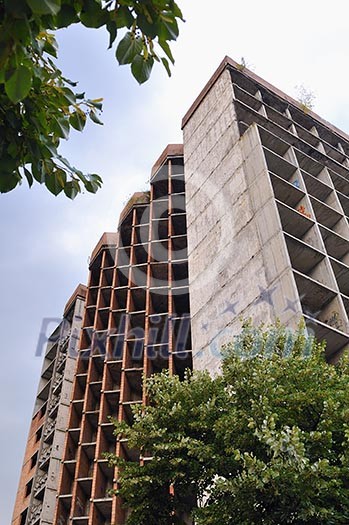 Building construction in city with blue sky in background and green trees in front Building construction in city with blue sky in background and green trees in front