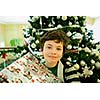 Smiling boy with giftbox looking at camera out of decorated firtree