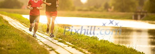 Couple running outdoors, at sunset, by a river, staying active and fit Couple running outdoors, at sunset, by a river, staying active and fit
