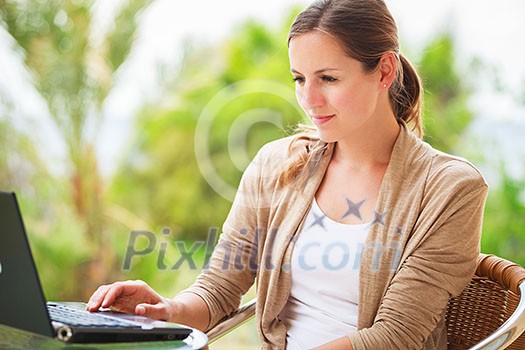 Portrait of a pretty young woman working on her computer on a terrace of her house