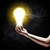 Close up image of human hand holding electrical bulb in darkness