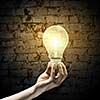 Close up image of human hand holding electrical bulb in darkness