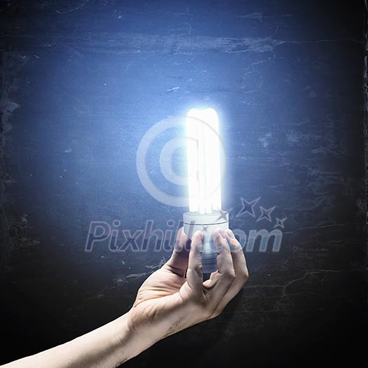 Close up image of human hand holding electrical bulb in darkness Close up image of human hand holding electrical bulb in darkness