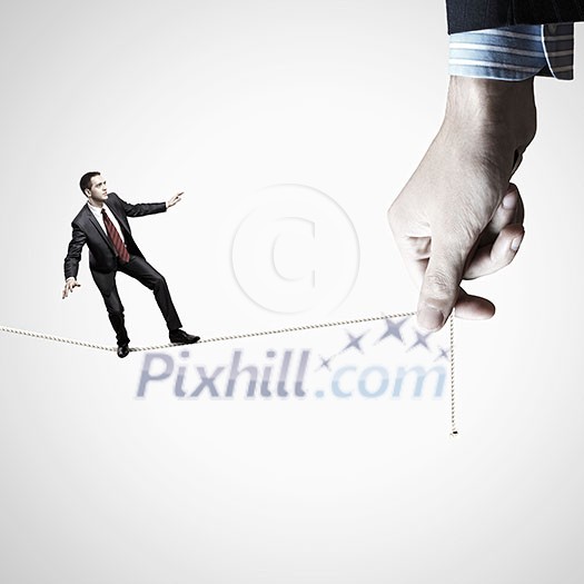 Young businessman balancing on rope controlled by male hand Young businessman balancing on rope controlled by male hand