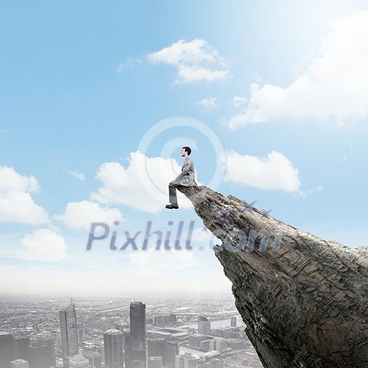 Young businessman sitting on edge of rock Young businessman sitting on edge of rock