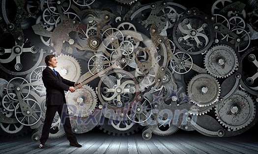 Young businessman fixing gears mechanism with wrench Young businessman fixing gears mechanism with wrench