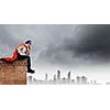 Thoughtful superman in cape and mask sitting on top of building