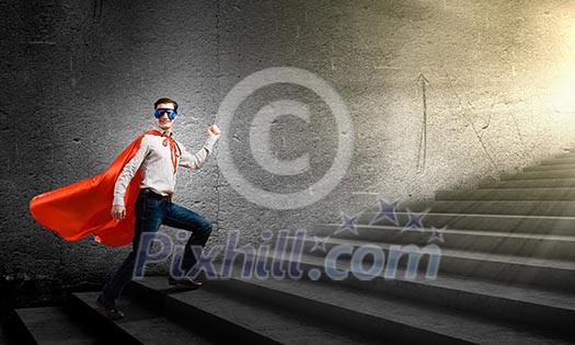 Young confident superman in mask and cape walking on ladder Young confident superman in mask and cape walking on ladder