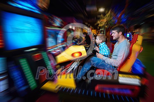 happy father and son playing driving wheel video game in playground theme park happy father and son playing driving wheel video game in playground theme park