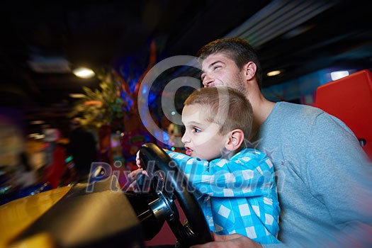 happy father and son playing driving wheel video game in playground theme park happy father and son playing driving wheel video game in playground theme park