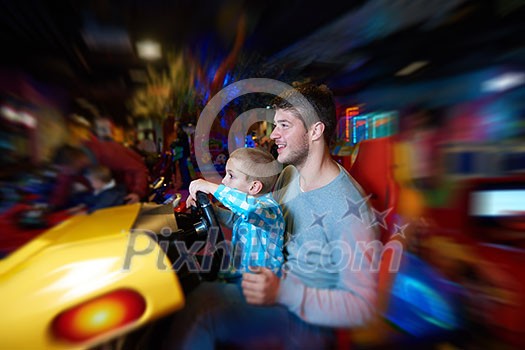 happy father and son playing driving wheel video game in playground theme park happy father and son playing driving wheel video game in playground theme park