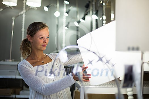 Pretty, young woman choosing the right light for her apartment in a modern home furnishings store (color toned image; shallow DOF) Pretty, young woman choosing the right light for her apartment in a modern home furnishings store (color toned image; shallow DOF)