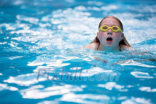 Young girl in goggles and cap swimming breast stroke style in the blue water pool Young girl in goggles and cap swimming breast stroke style in the blue water pool