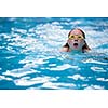 Young girl in goggles and cap swimming breast stroke style in the blue water pool