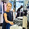 Beautiful young female shopper in a clothing store, chossing a blouse/t-shirt/garments (shallow DOF; color toned image)