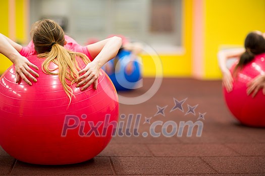 Group people in a pilates class at the gym - young woman with gymball at fitness training (shallow DOF, color toned image)